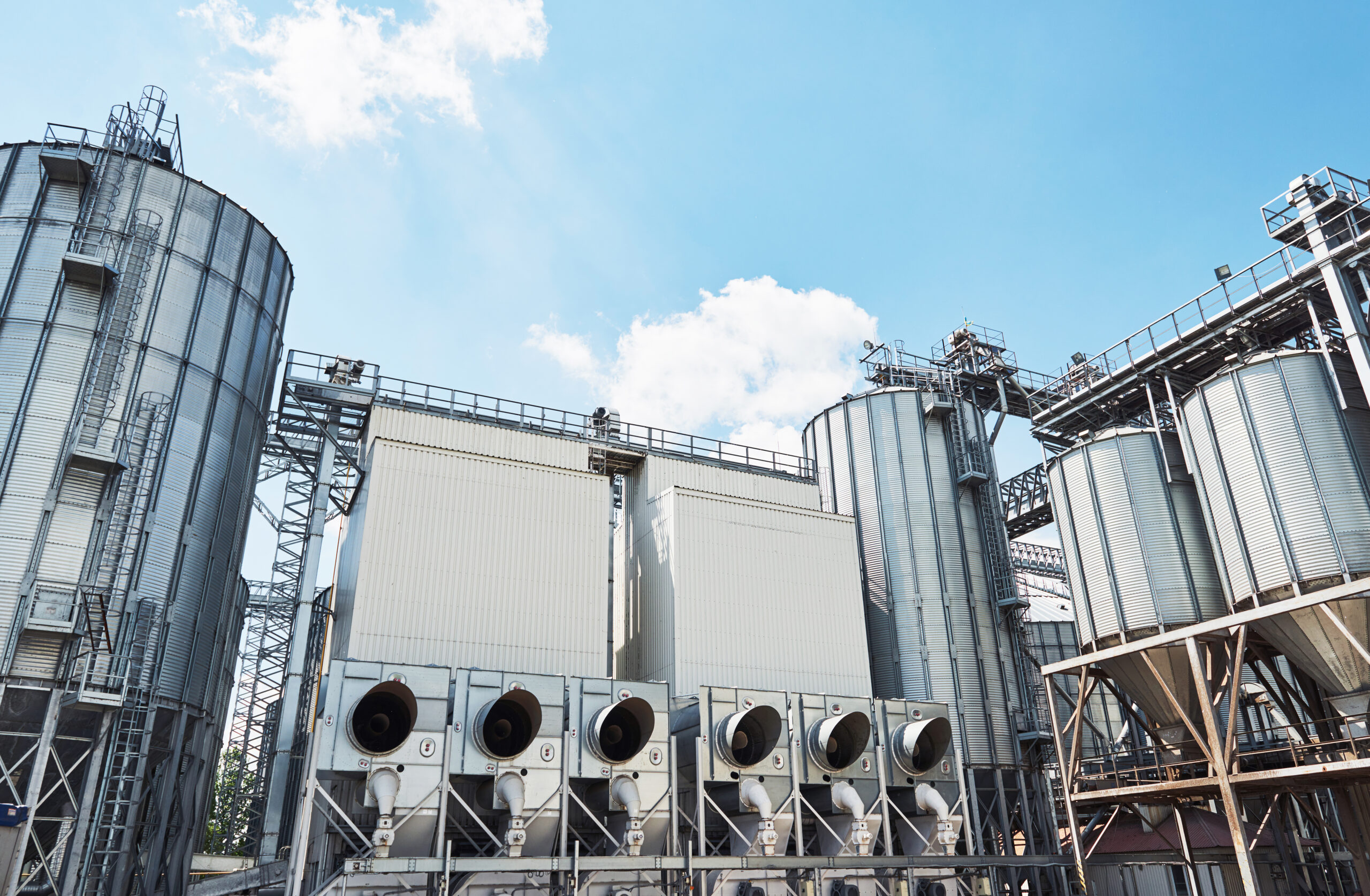 Agricultural Silos. Building Exterior. Storage and drying of grains, wheat, corn, soy, sunflower against the blue sky with white clouds